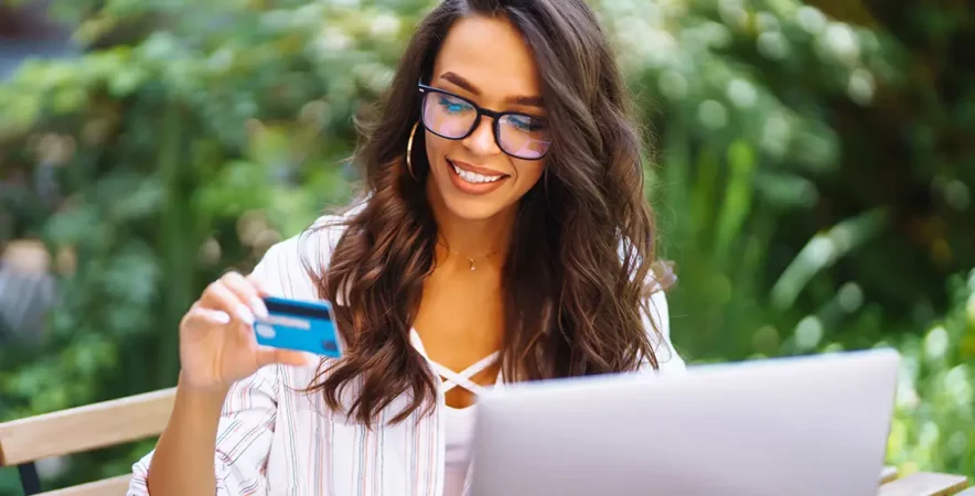 A person is holding their credit card while making an online payment at a laptop.