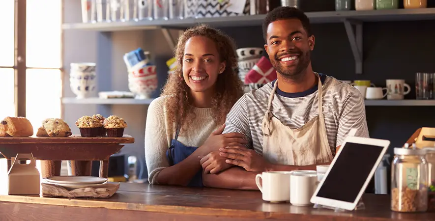 Two cafe owners stand next to their tablet POS terminal happy with their low processing rates.