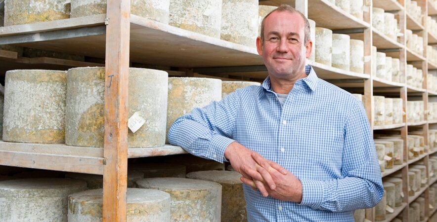 A cheese shop owner standing in a cellar smiling after switching payment processing service providers.