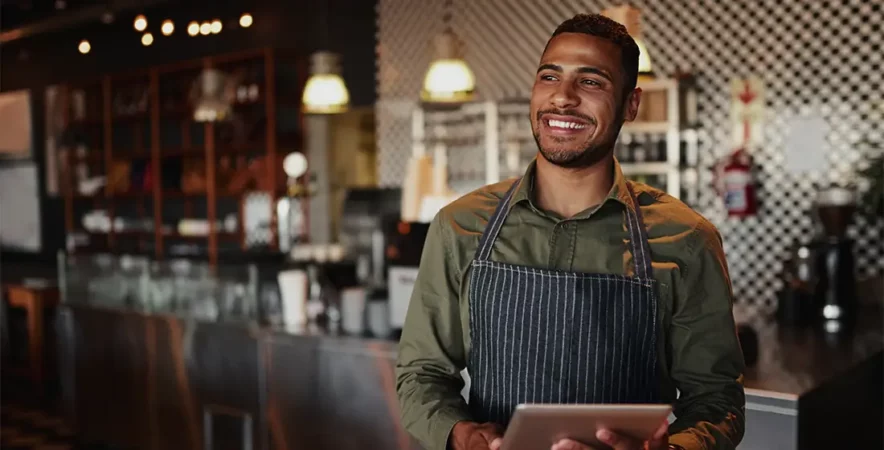 Owner holding a digital tablet while standing in a cafe reading the restaurant POS guide.