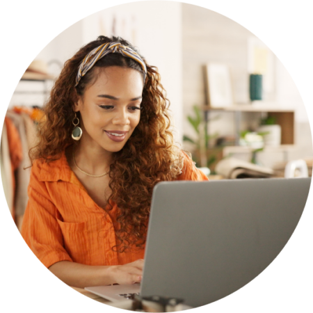 person with long curly hair wearing a orange-shirt using a laptop and smiling