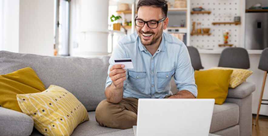 person using credit card and laptop to make an online purchase from their living room